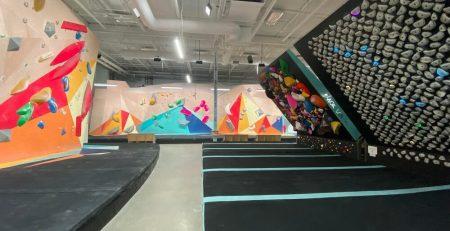 Indoor climbing facility. Various hand holds looking like rocks. One wall slanted inwards.