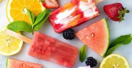 Homemade popsicles surrounded by orange and kiwi slices, watermelon, blackberries, peaches and strawberries