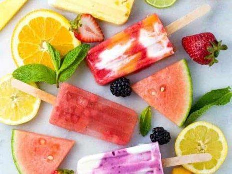 Homemade popsicles surrounded by orange and kiwi slices, watermelon, blackberries, peaches and strawberries