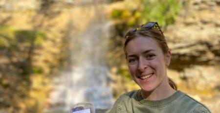 Hiker in front of a blurry waterfall. Holding a small container of food with a label on the top