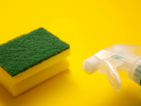Green scrub pad with the top portion of a spray bottle on a yellow background